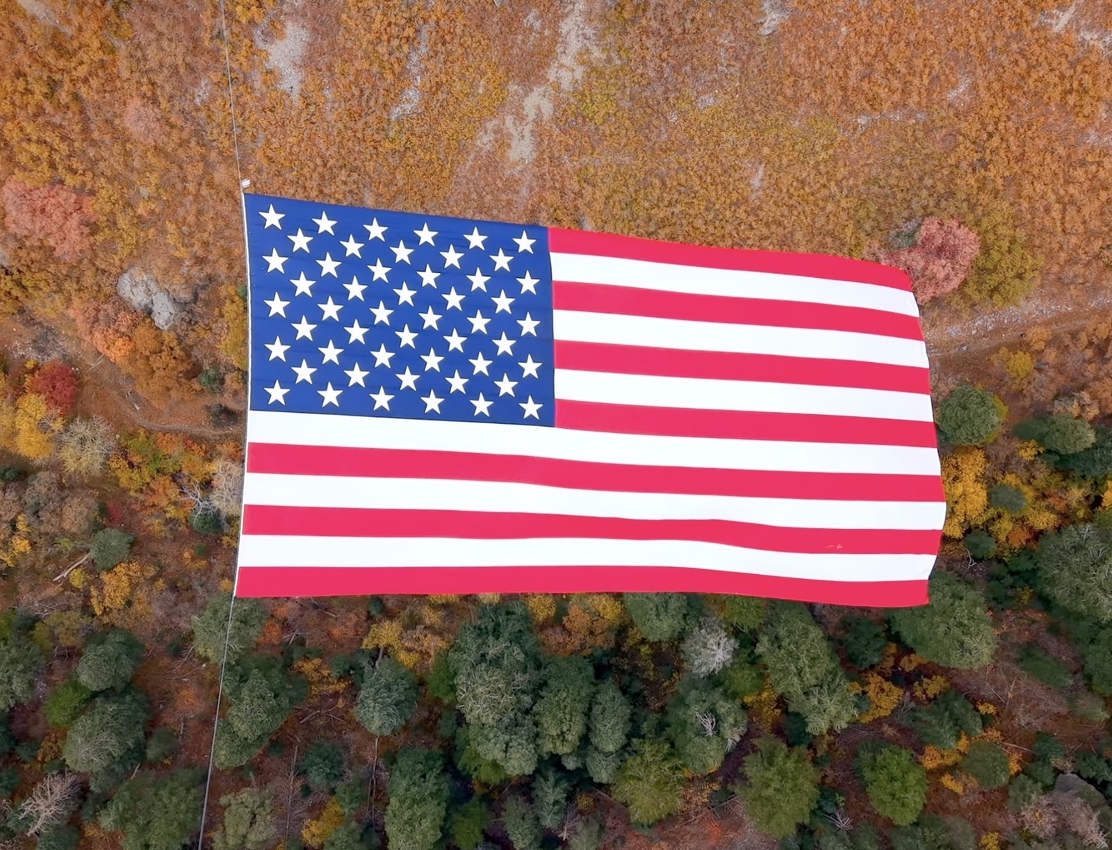 Top-down drone view of the entire flag floating above autumn treetops.