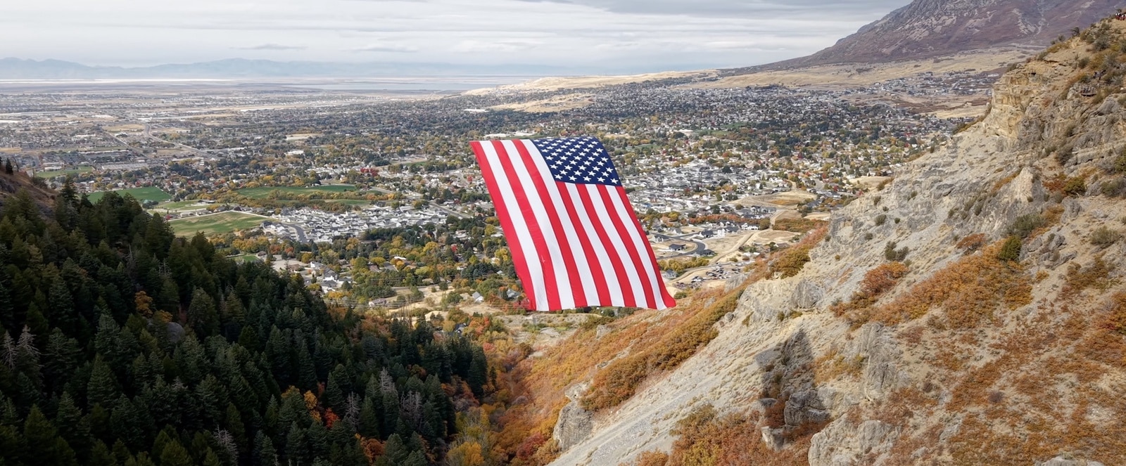 Flag hanging above the canyon with Ogden neighborhoods and distant mountains behind.