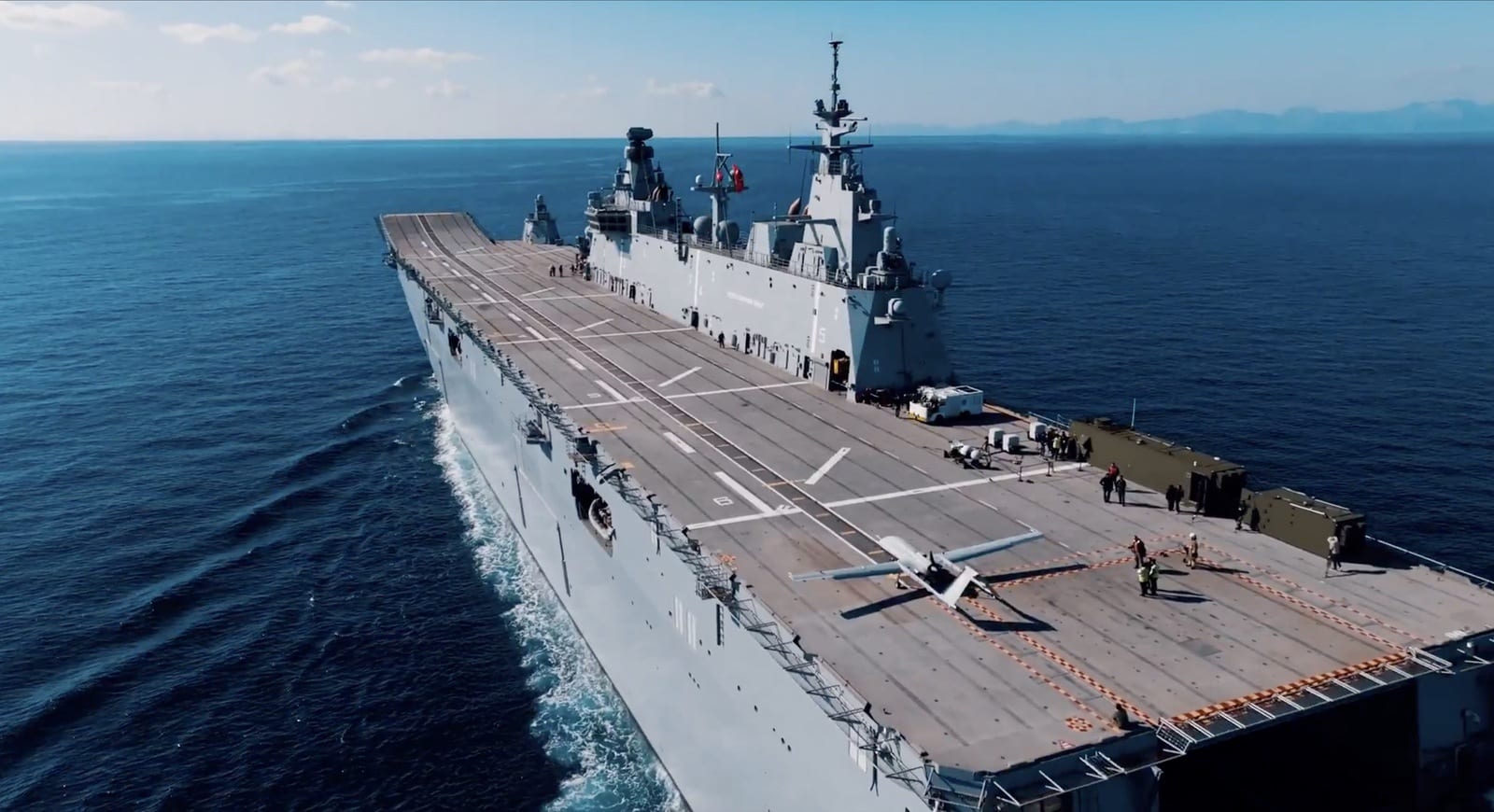 Aerial view along the full flight deck of TCG Anadolu with a drone parked aft.