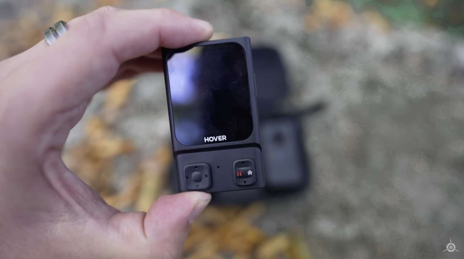 Hand holding the small HoverAir Beacon remote with its color touchscreen dark.