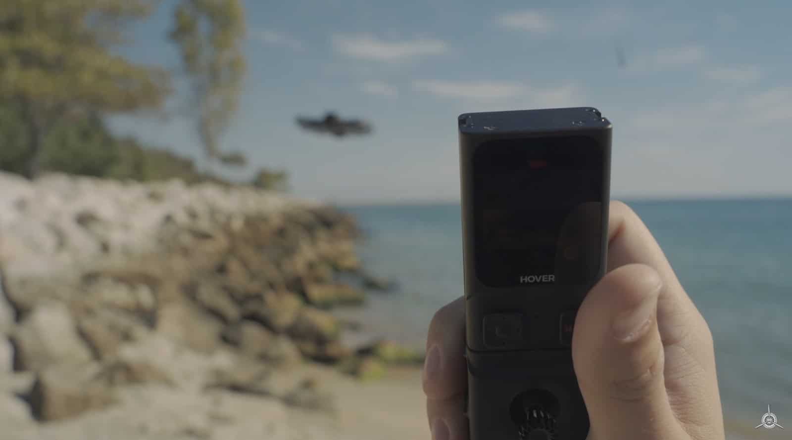 Hand raising the Beacon at a rocky lakeshore as the drone hovers behind.