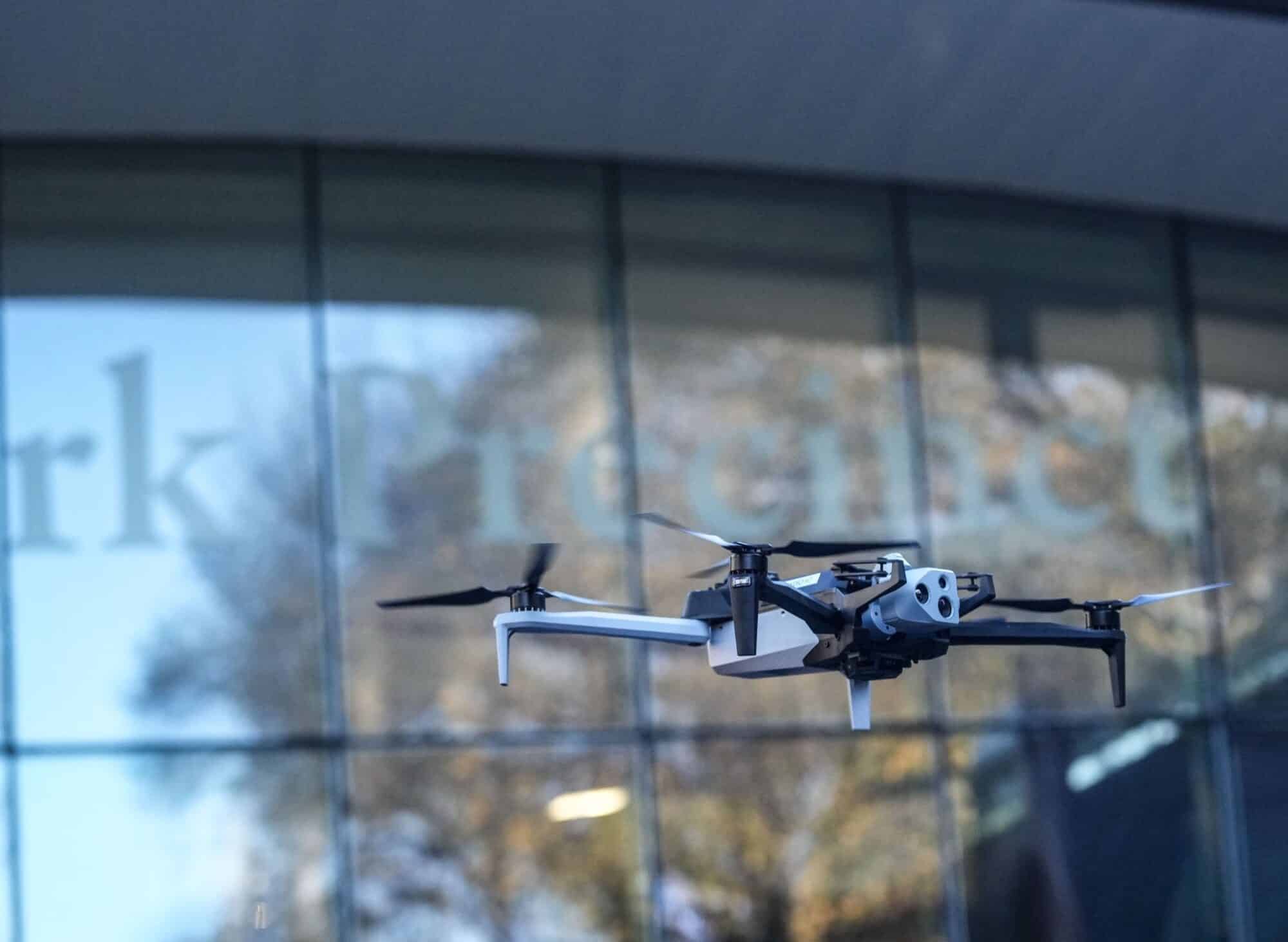 A Skydio drone hovers in front of a reflective glass office facade.
