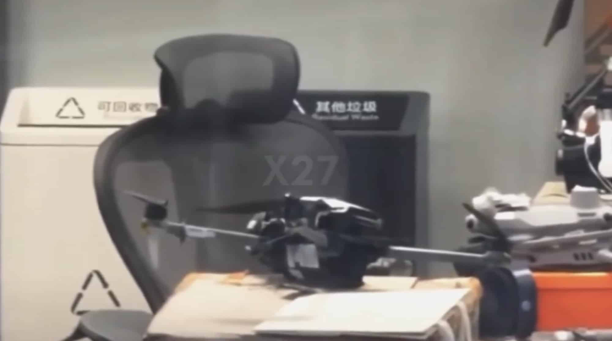 Blurred frame showing a prototype drone resting on a desk inside an office.