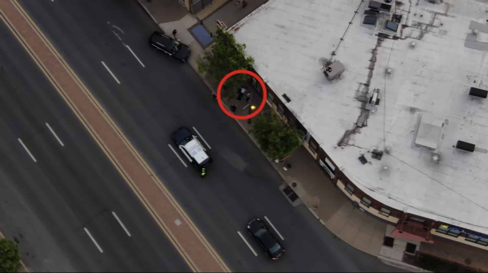 Aerial police drone frame with a red circle marking a person beside a roadway.