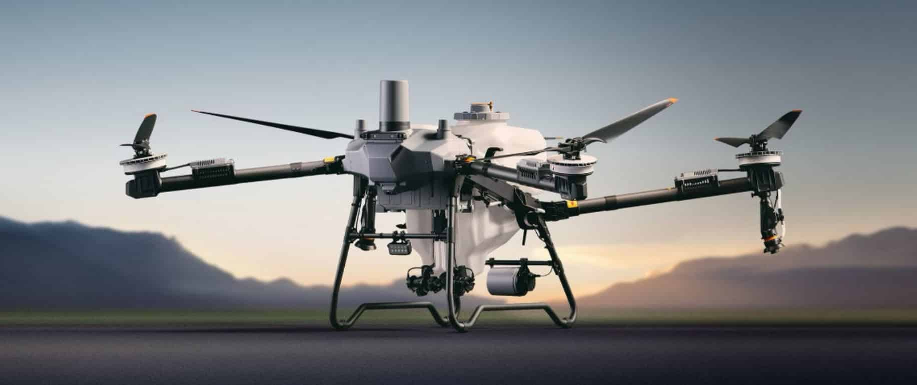 Agras T100 spraying drone hovering above a field at dusk.