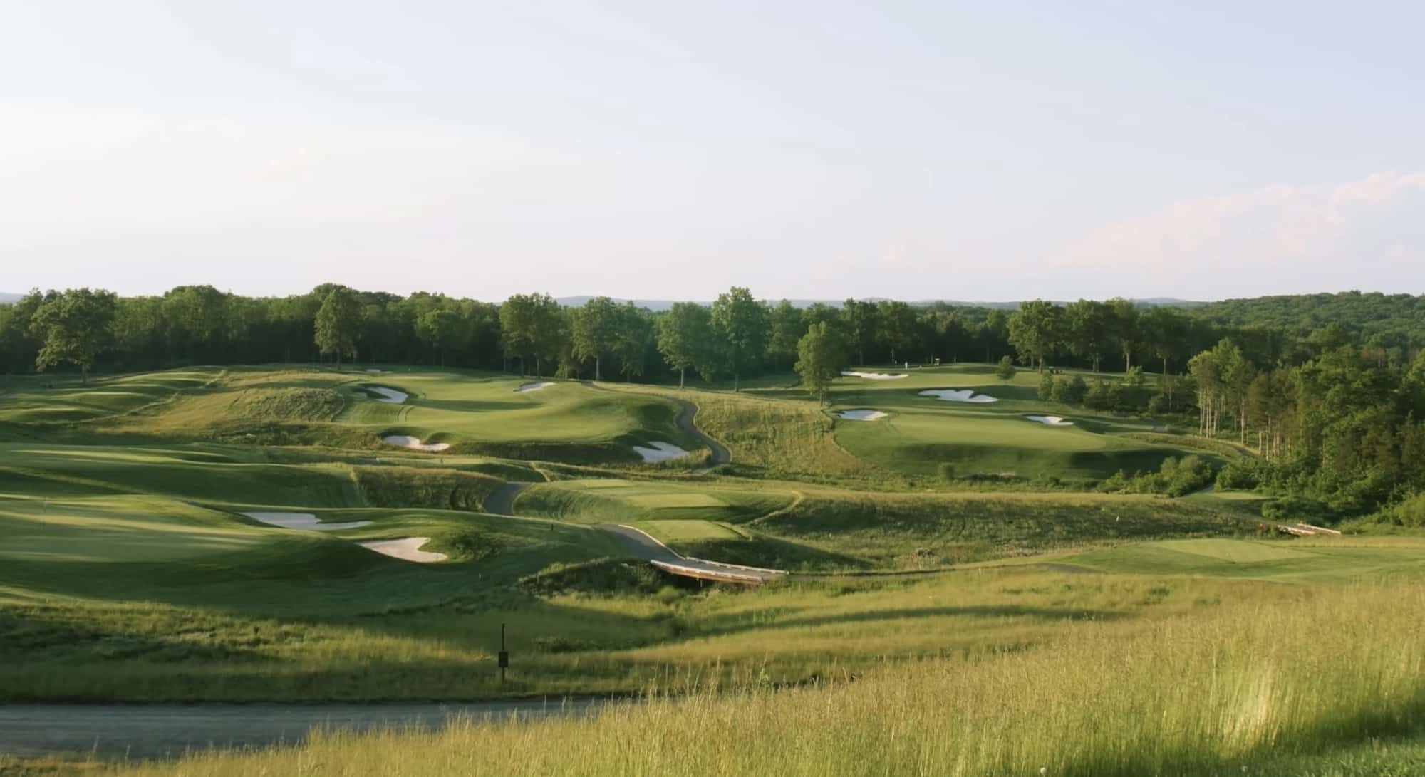 Aerial view of a manicured golf course ringed by dense summer forest.