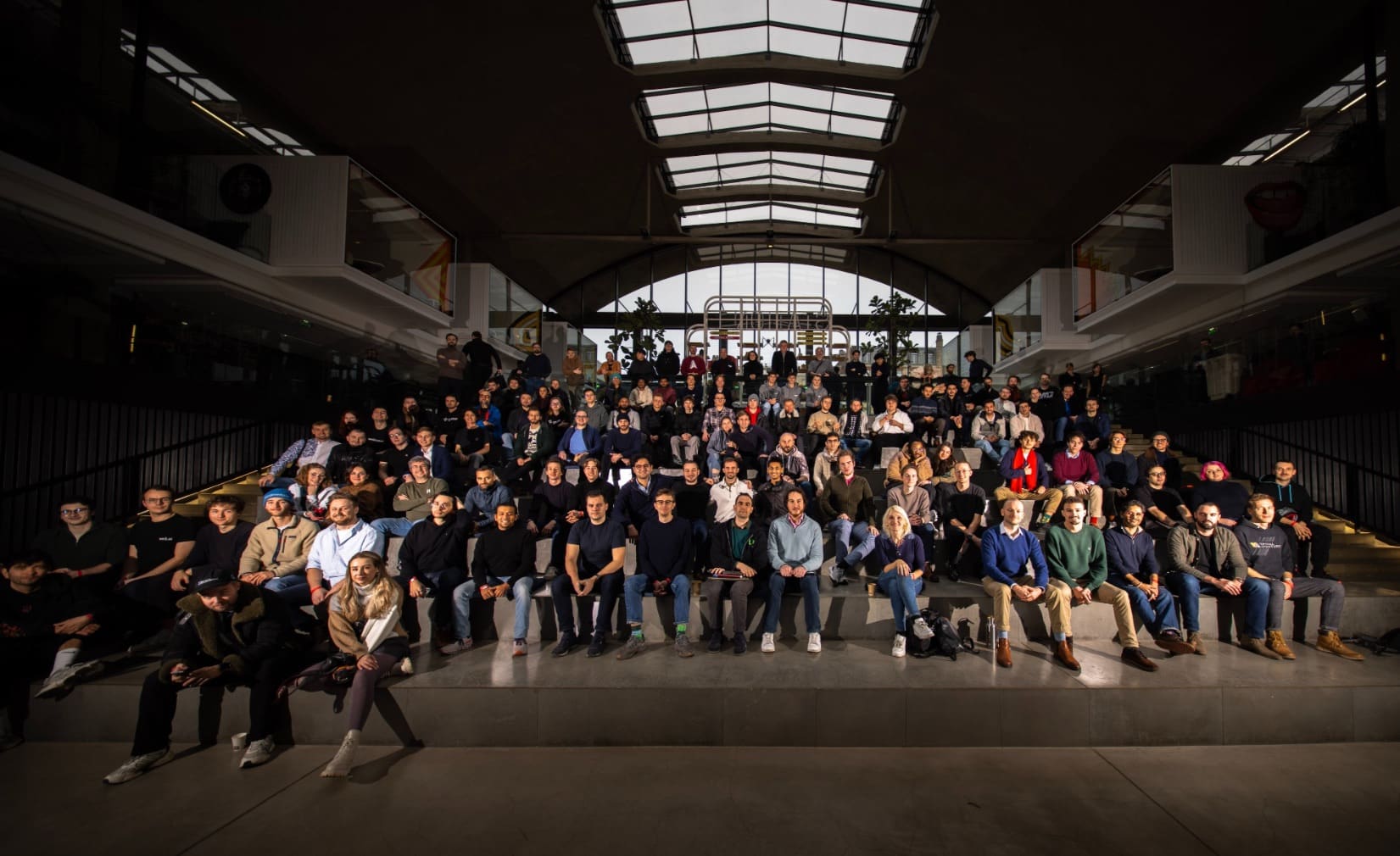 Large group portrait of defense tech hackathon participants inside a Paris hall.