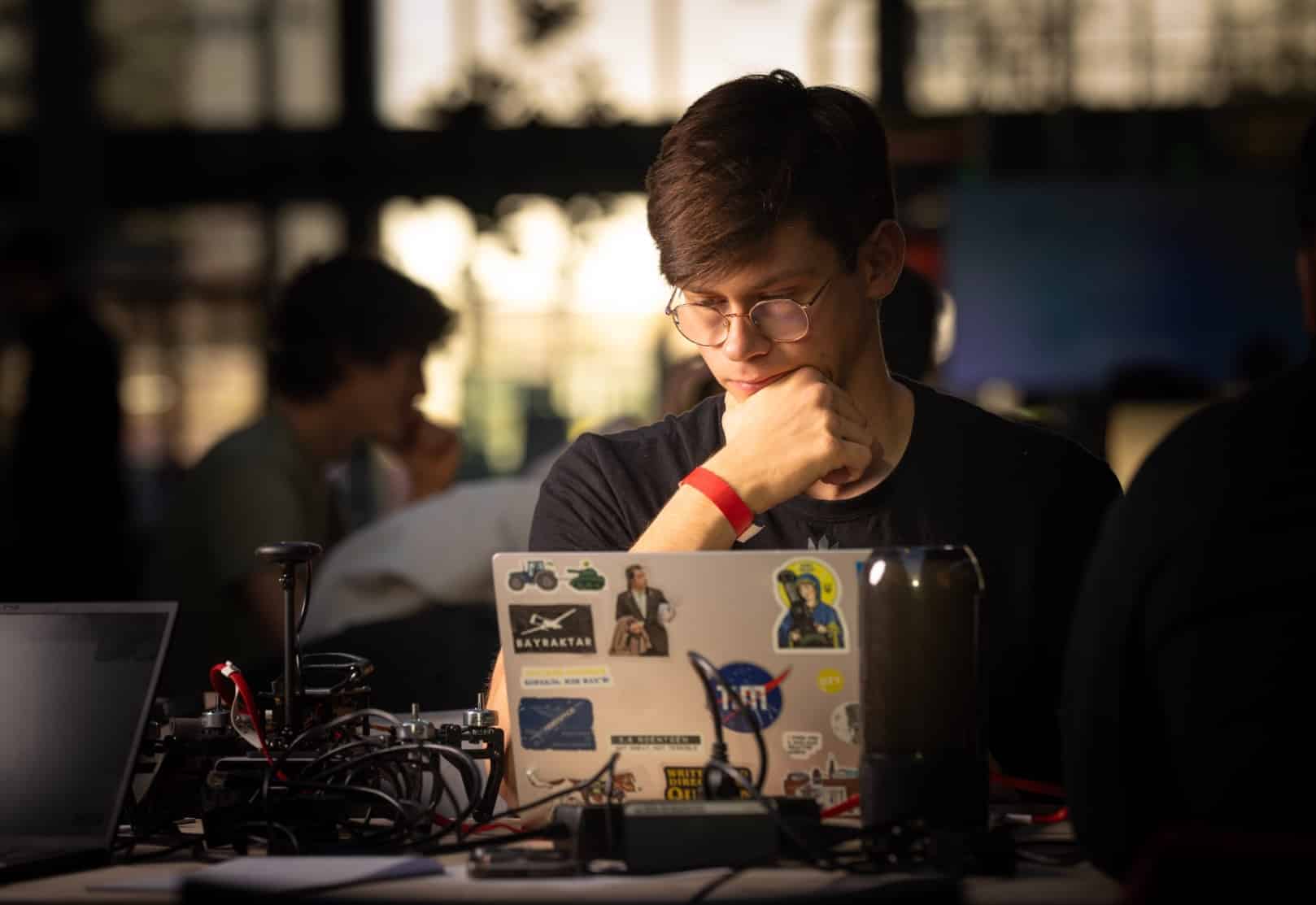 Hackathon participant working on a laptop beside drone electronics and wiring.