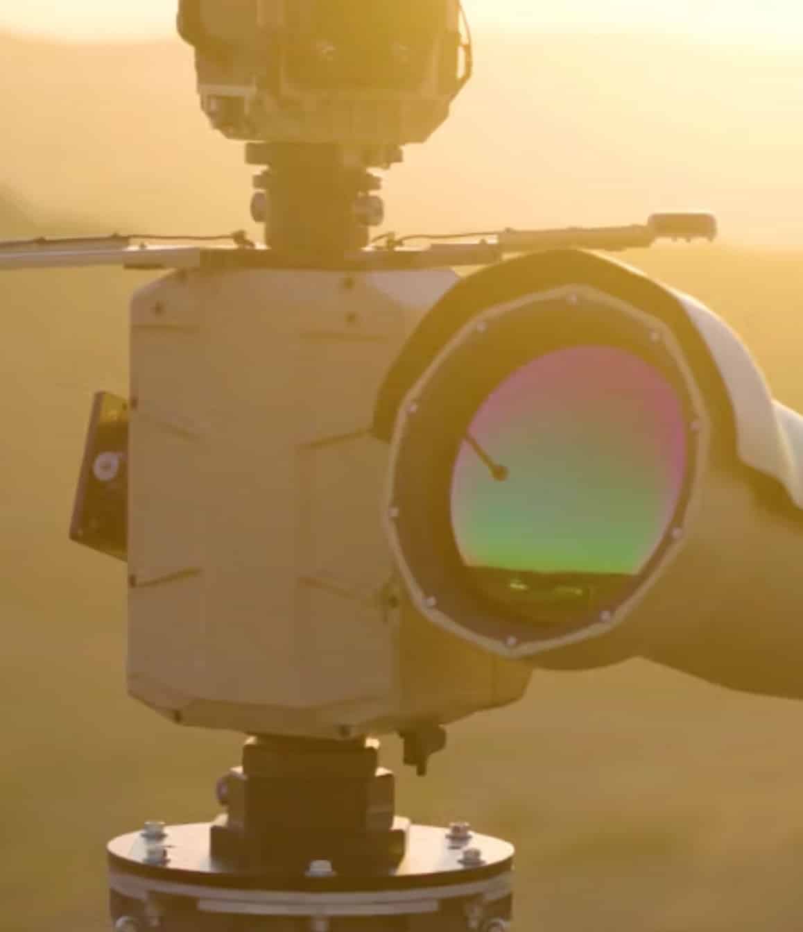 Close-up of an electro-optical sensor turret on its mount against a hazy sky.