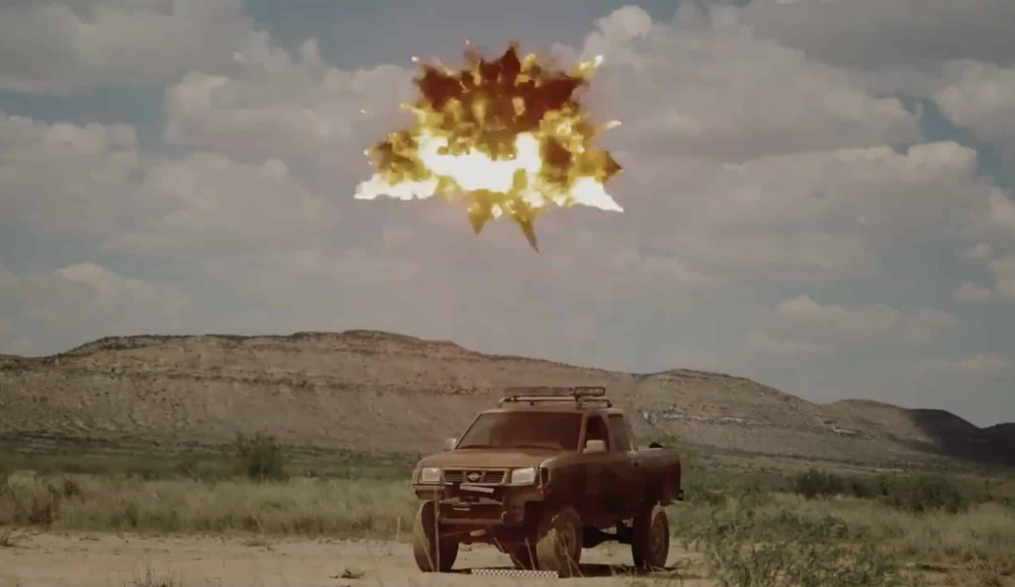 Airburst explosion above a desert road with a pickup truck below during testing.