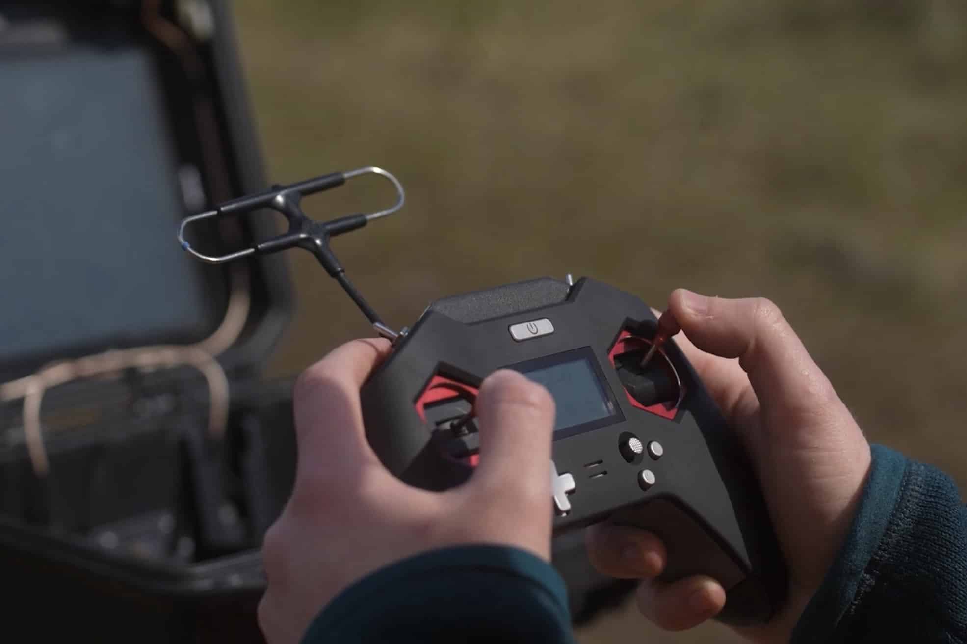 Hands gripping a black drone remote with its antenna raised in a field.