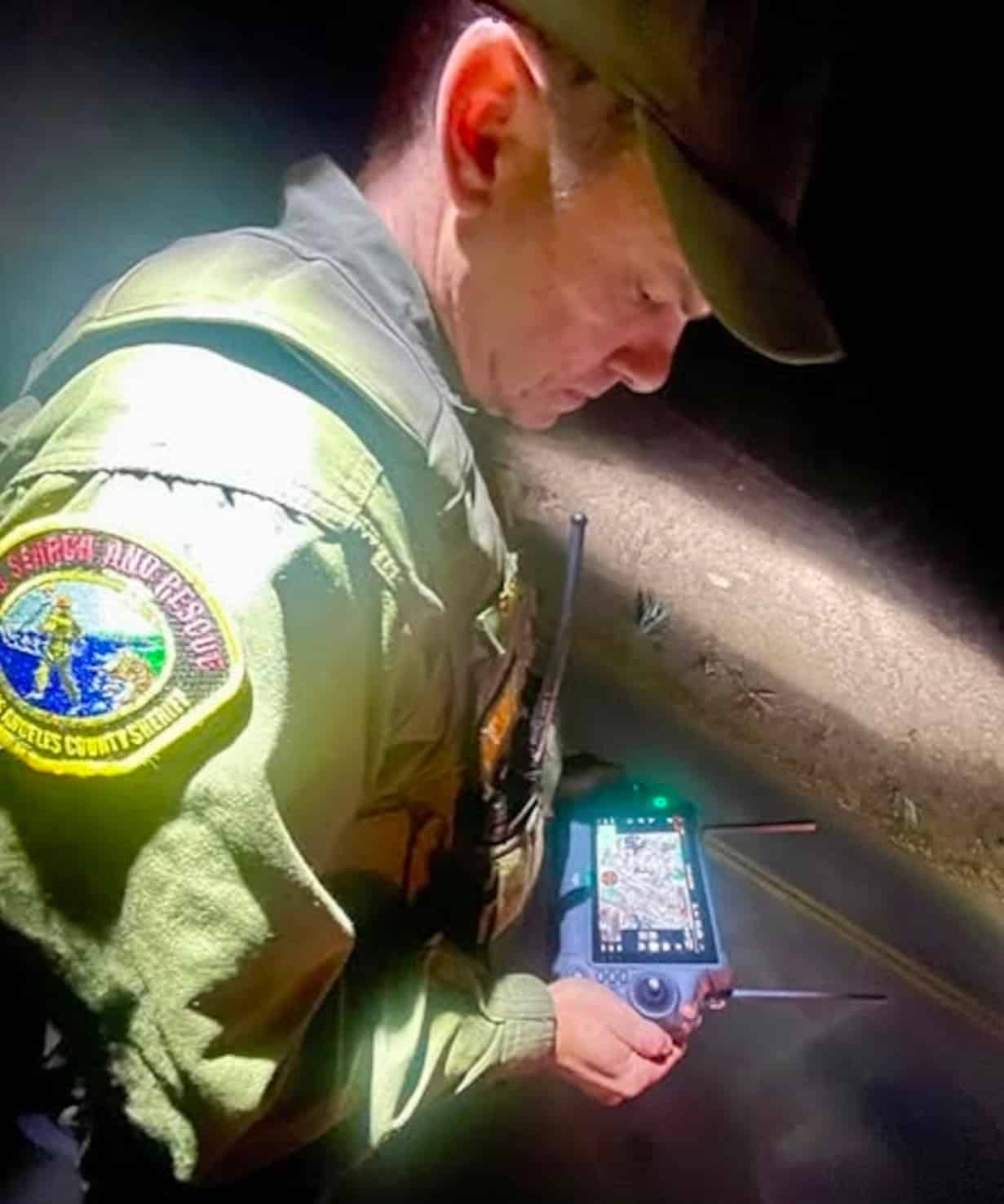 Sheriff search and rescue deputy working a drone controller with a map screen at night.