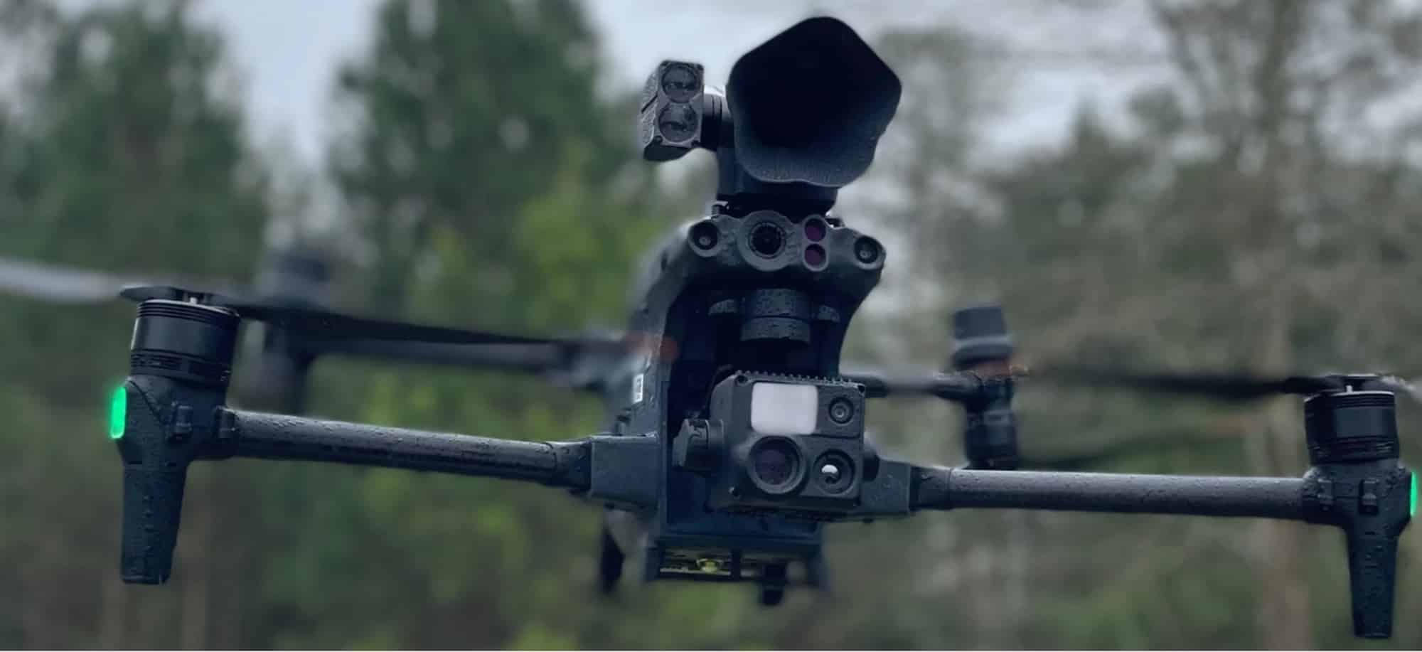 DJI Matrice hovering at low level with its thermal gimbal and spotlight fitted.