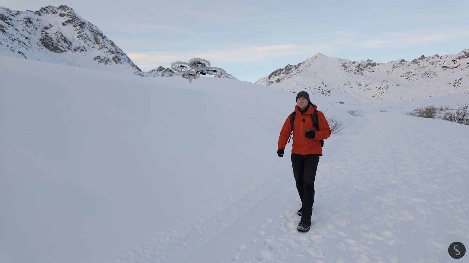 DJI Flip hovering above a hiker in a red parka on a snowy trail.