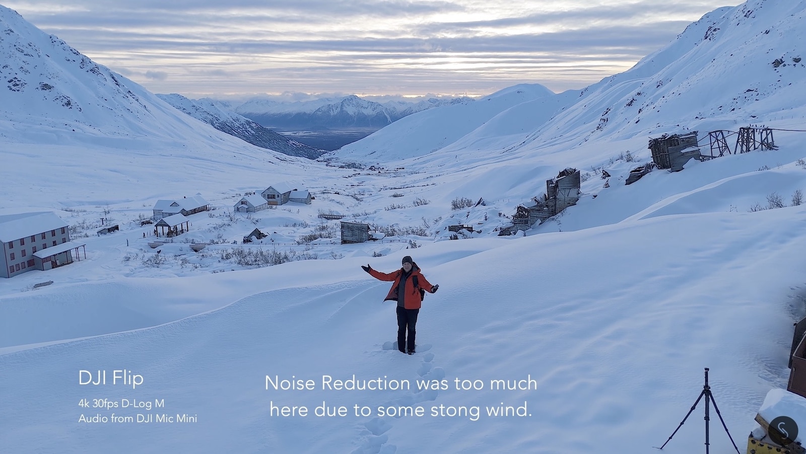 Pilot waving in a snowbound valley beside an abandoned mining camp.