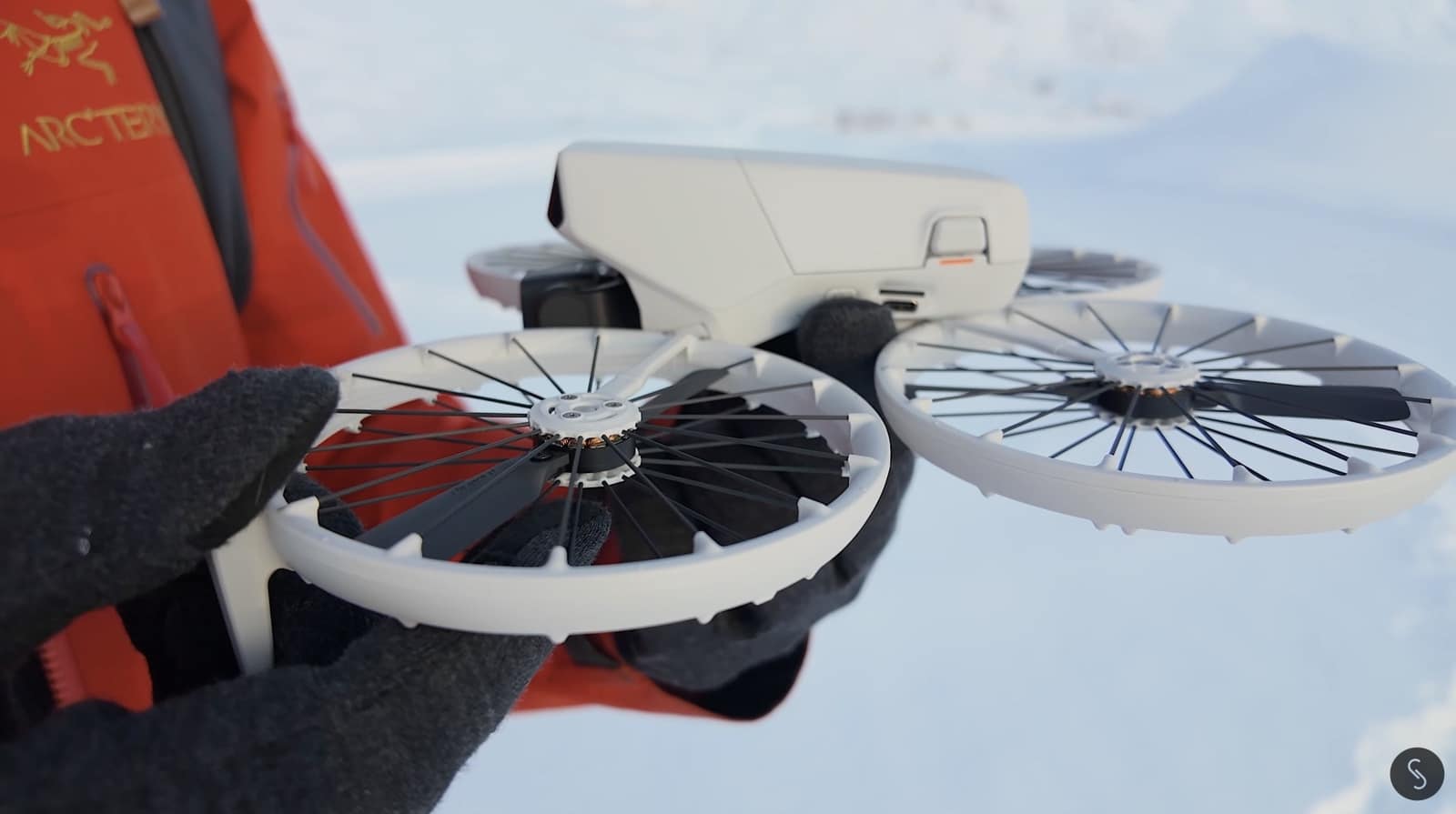 Gloved hand holding the white DJI Flip with its propeller cages unfolded in snow.