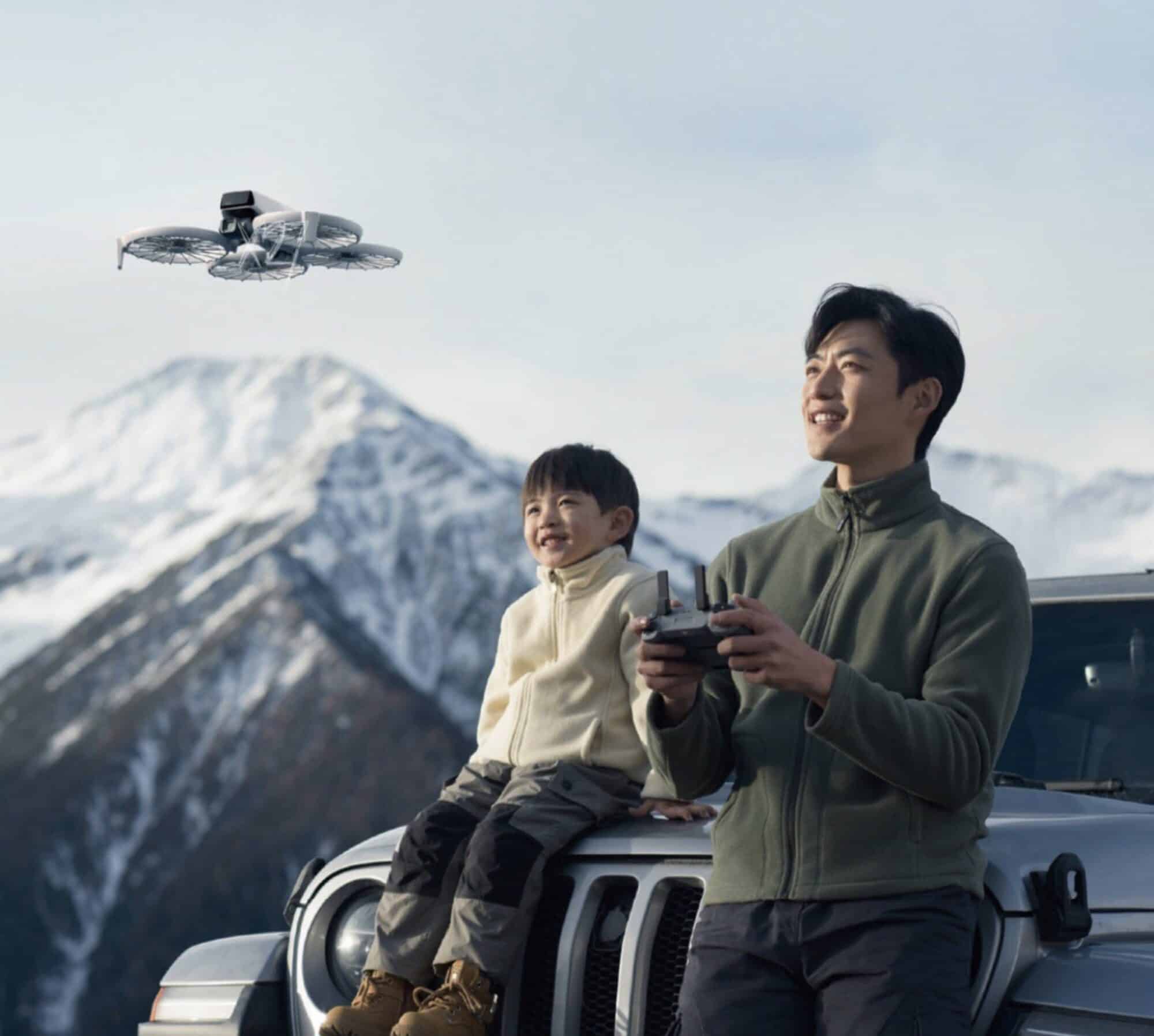 Adult and child fly a DJI Flip from a car hood below snowy mountains.