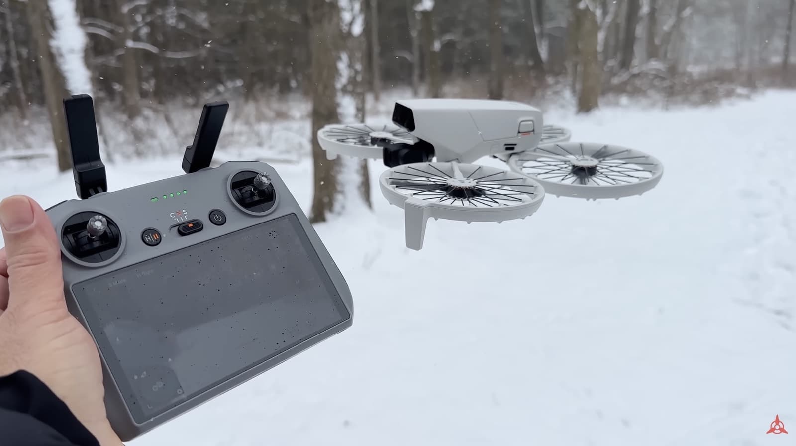 Hand holds the controller as the Flip hovers above a snowy woodland trail.