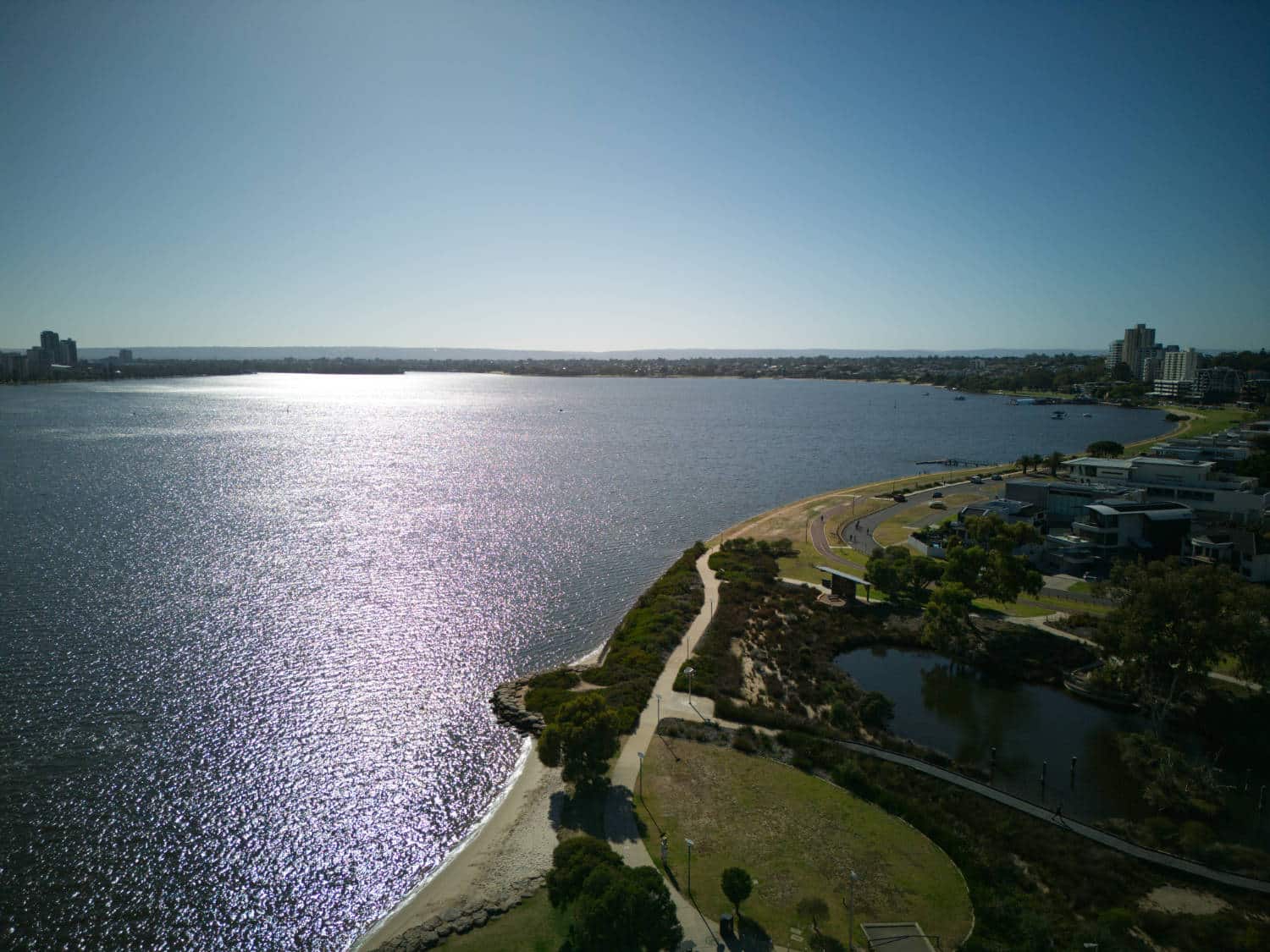Aerial shot into the sun across the river with a wooded park on the shore.