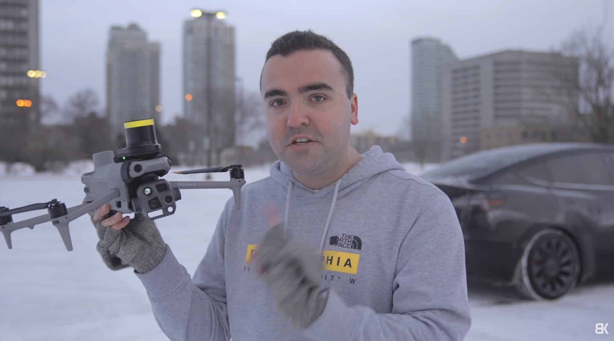 Billy Kyle holding the DJI Matrice 4T in the snow with city towers behind.