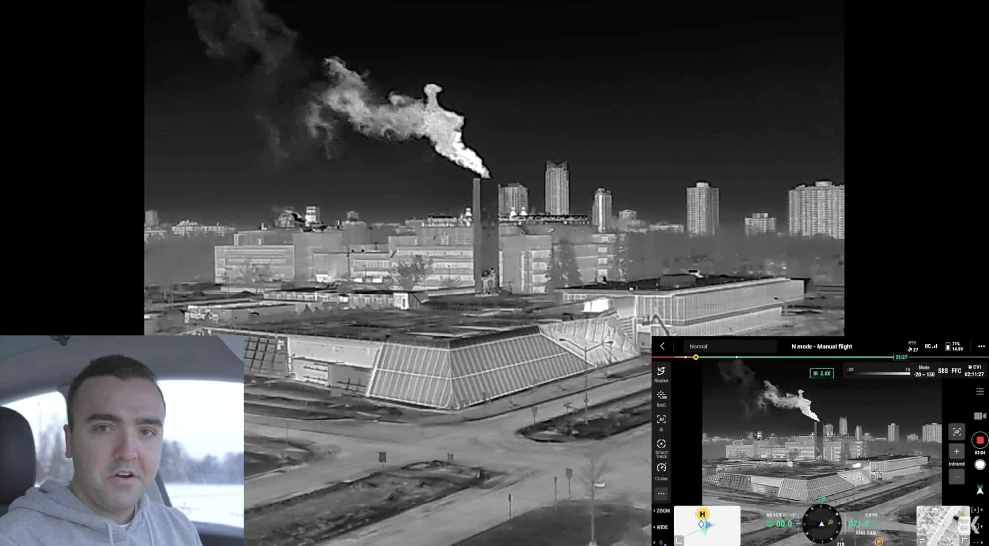 Infrared view of a steaming smokestack over a snowy city, pilot inset at corner.