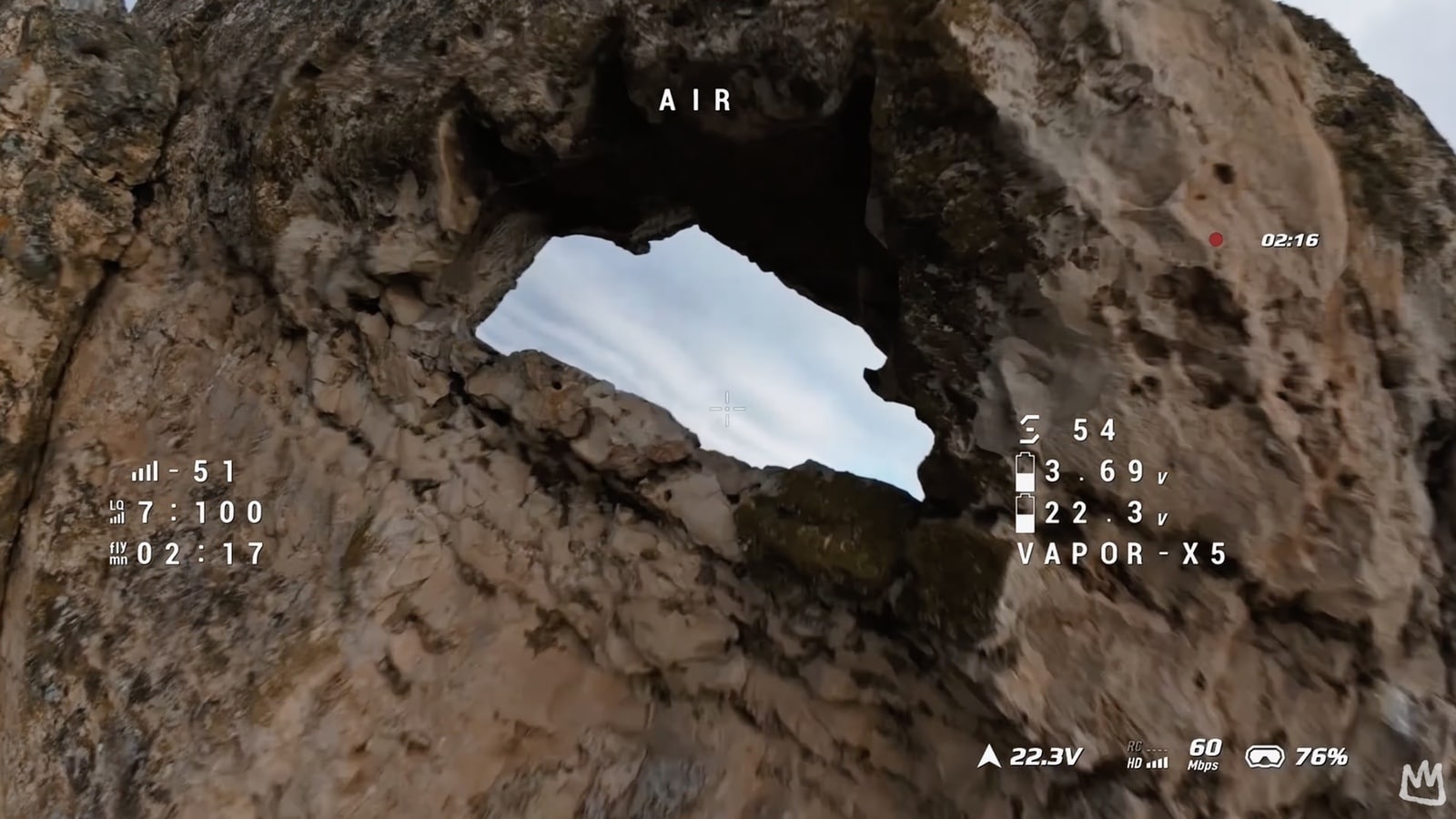 Closer FPV pass at the pierced rock arch with signal and voltage readouts.