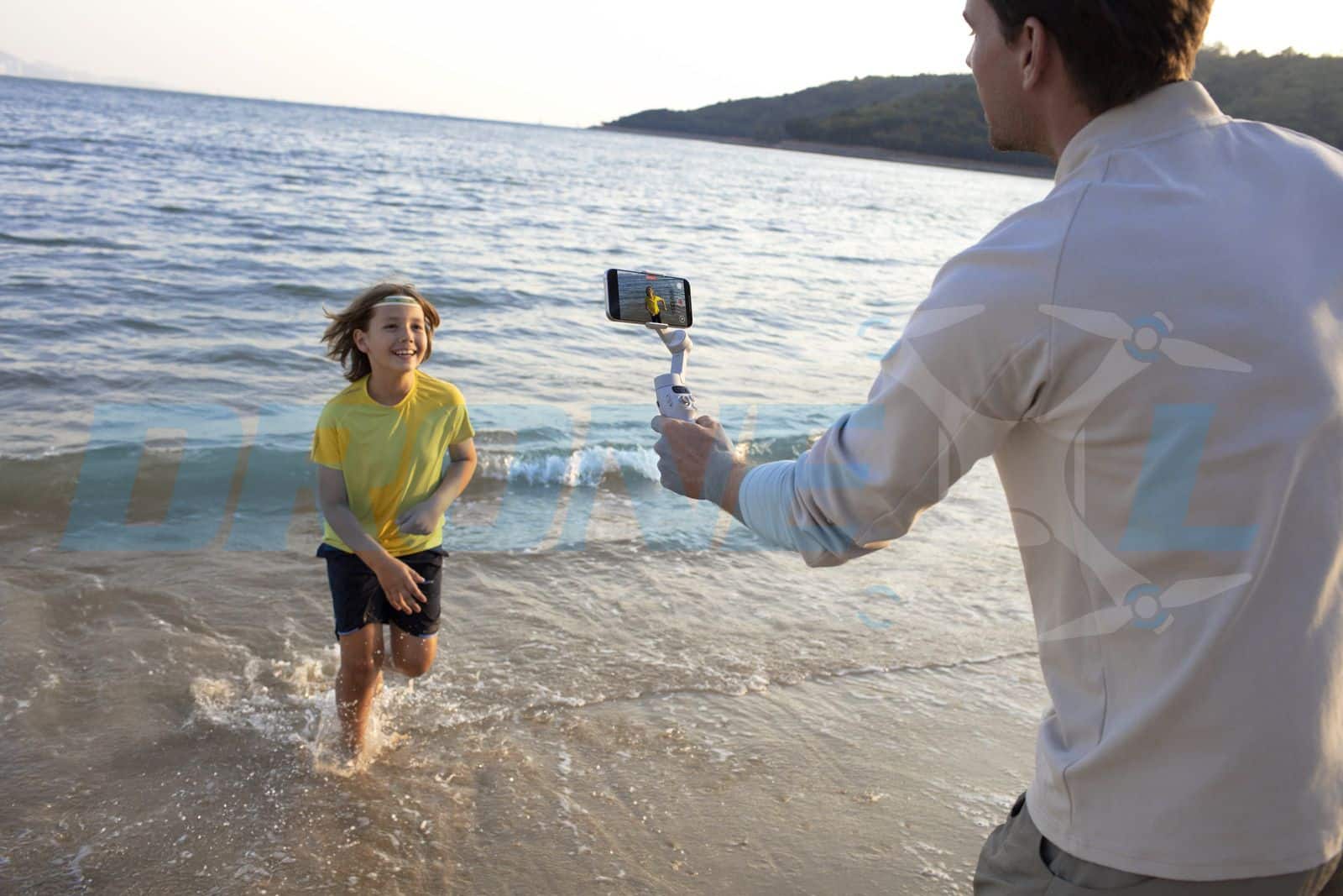Wading child filmed from behind by an adult holding the white gimbal at the shore.