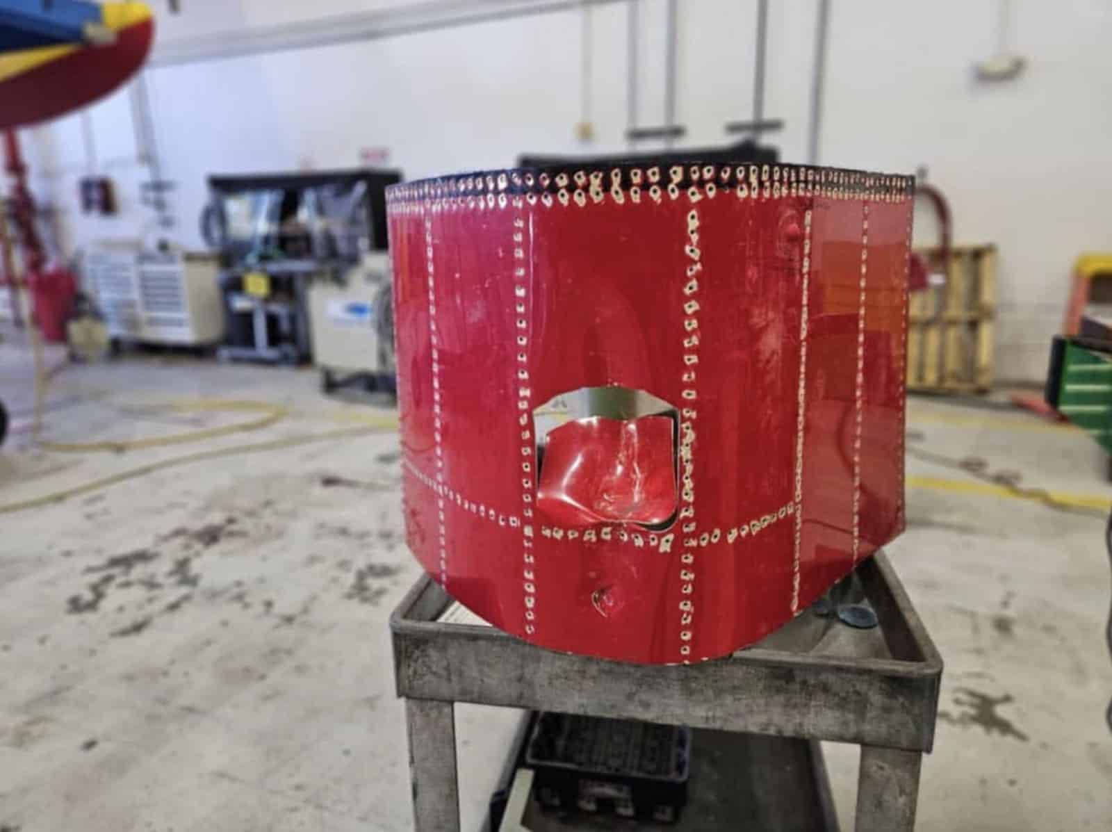 The punctured red wingtip skin panel removed and propped on a workshop stand.