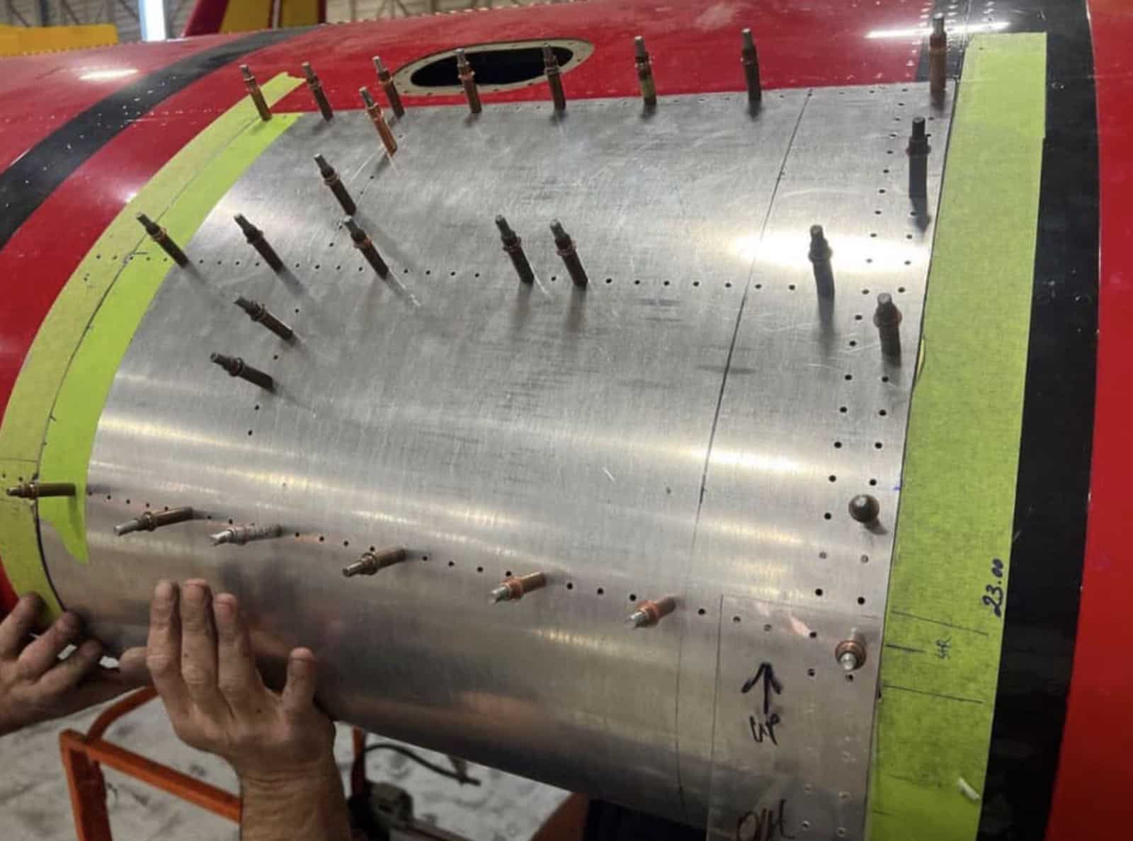 A technician holds a bare aluminium replacement skin against the wingtip.