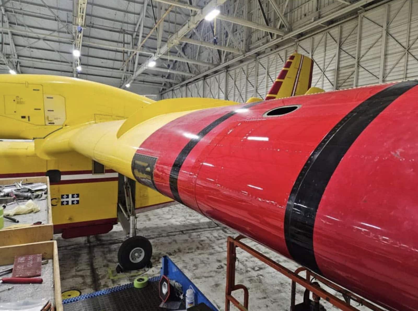 The Quebec water bomber sits in a hangar with its wing under repair.