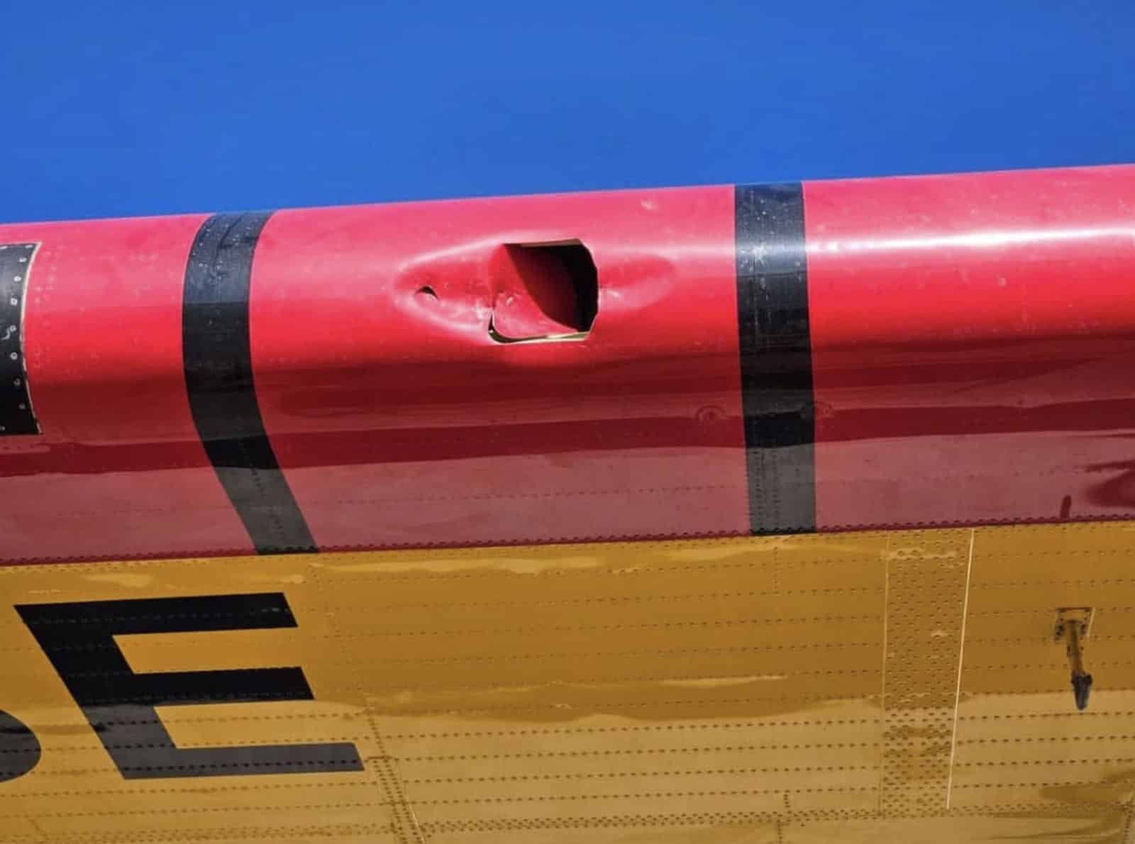 The ragged hole punched through the red wing skin, seen against blue sky.
