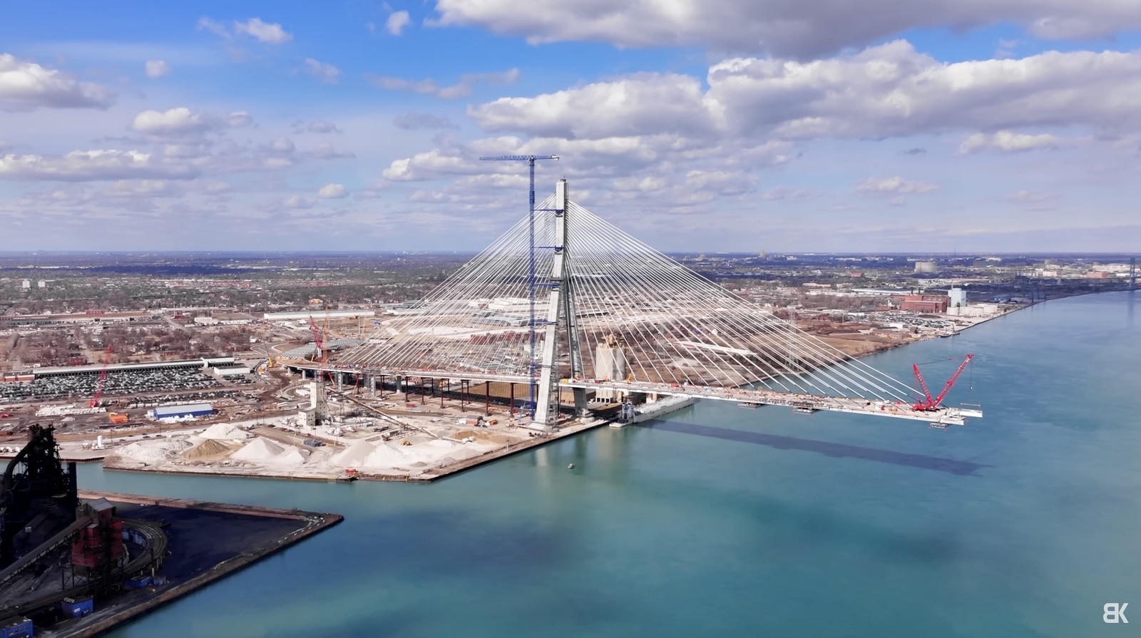Aerial view of a cable-stayed bridge under construction beside a working river port.