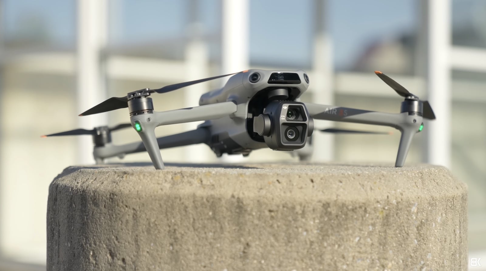 A DJI Air 3S rests on a concrete pillar outside a glass building.