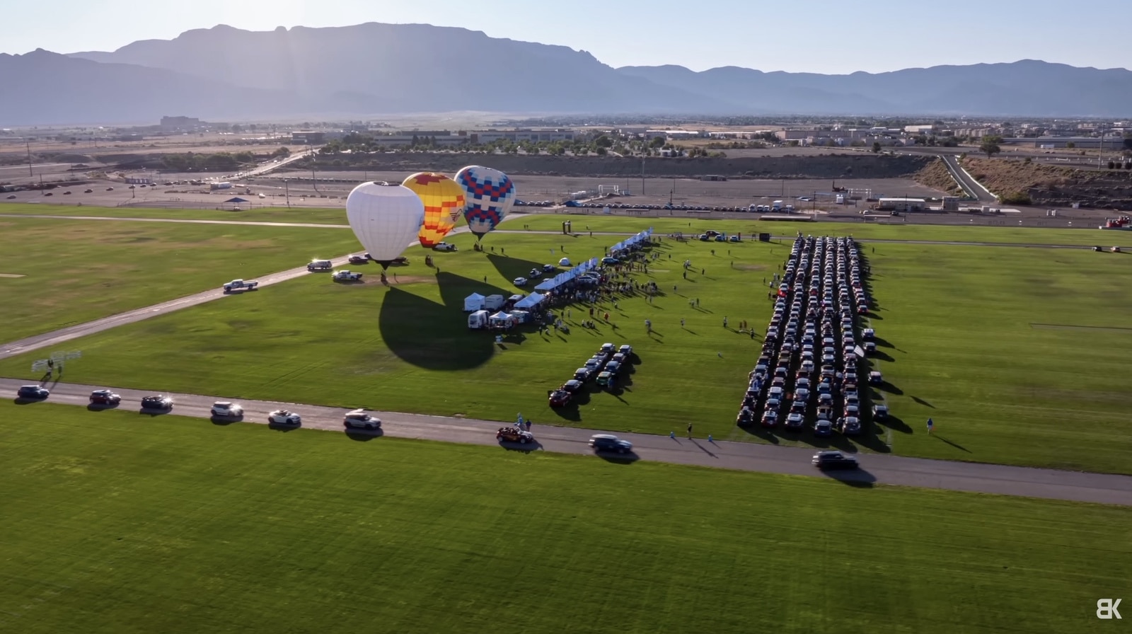 Aerial view of hot-air balloons and hundreds of parked Mini Coopers ranked across a field.