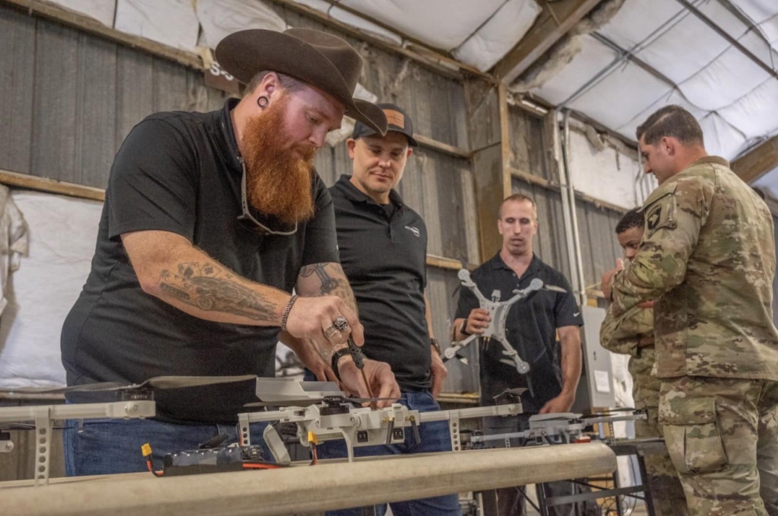 Soldiers and technicians assemble 3D printed drone parts on a hangar workbench.