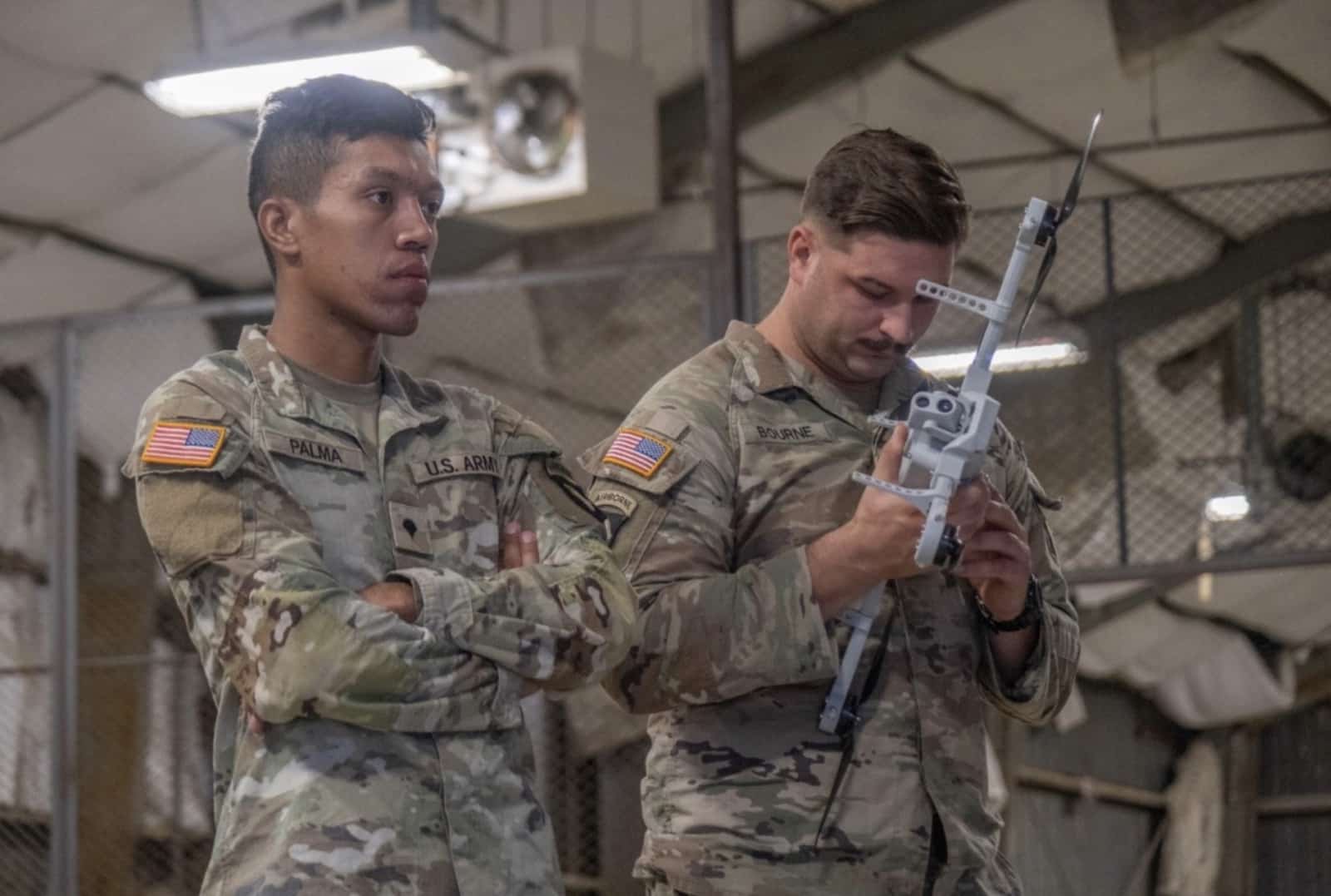 Two US Army soldiers inspect a 3D printed drone airframe indoors.
