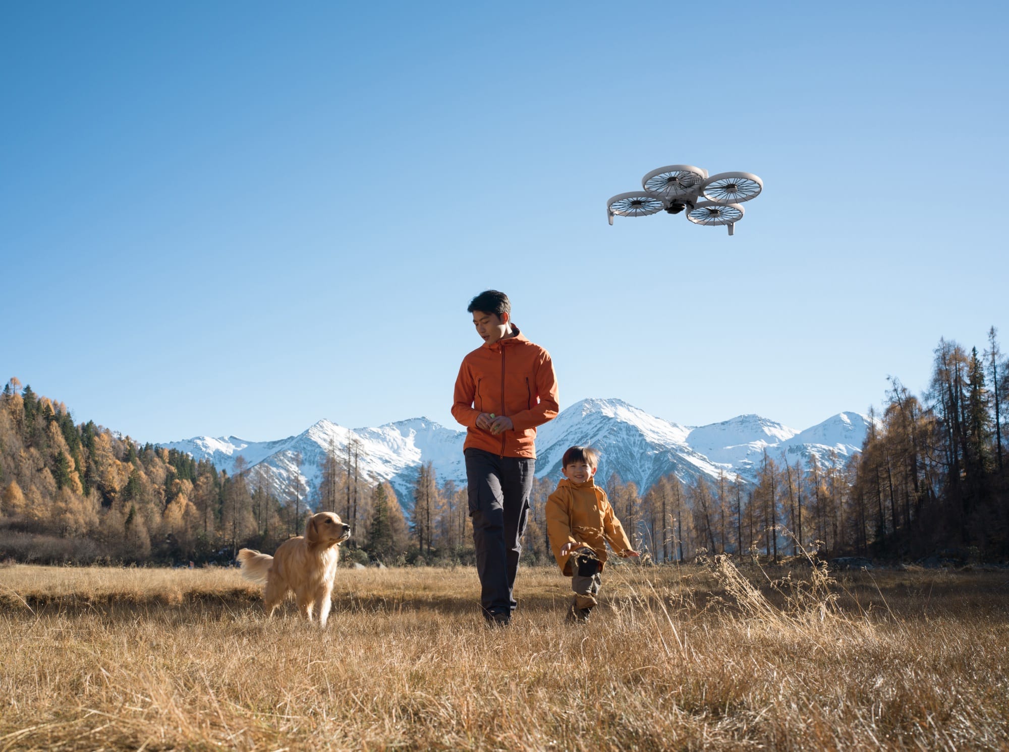 DJI Flip hovering above a man, child and golden retriever in a mountain meadow.
