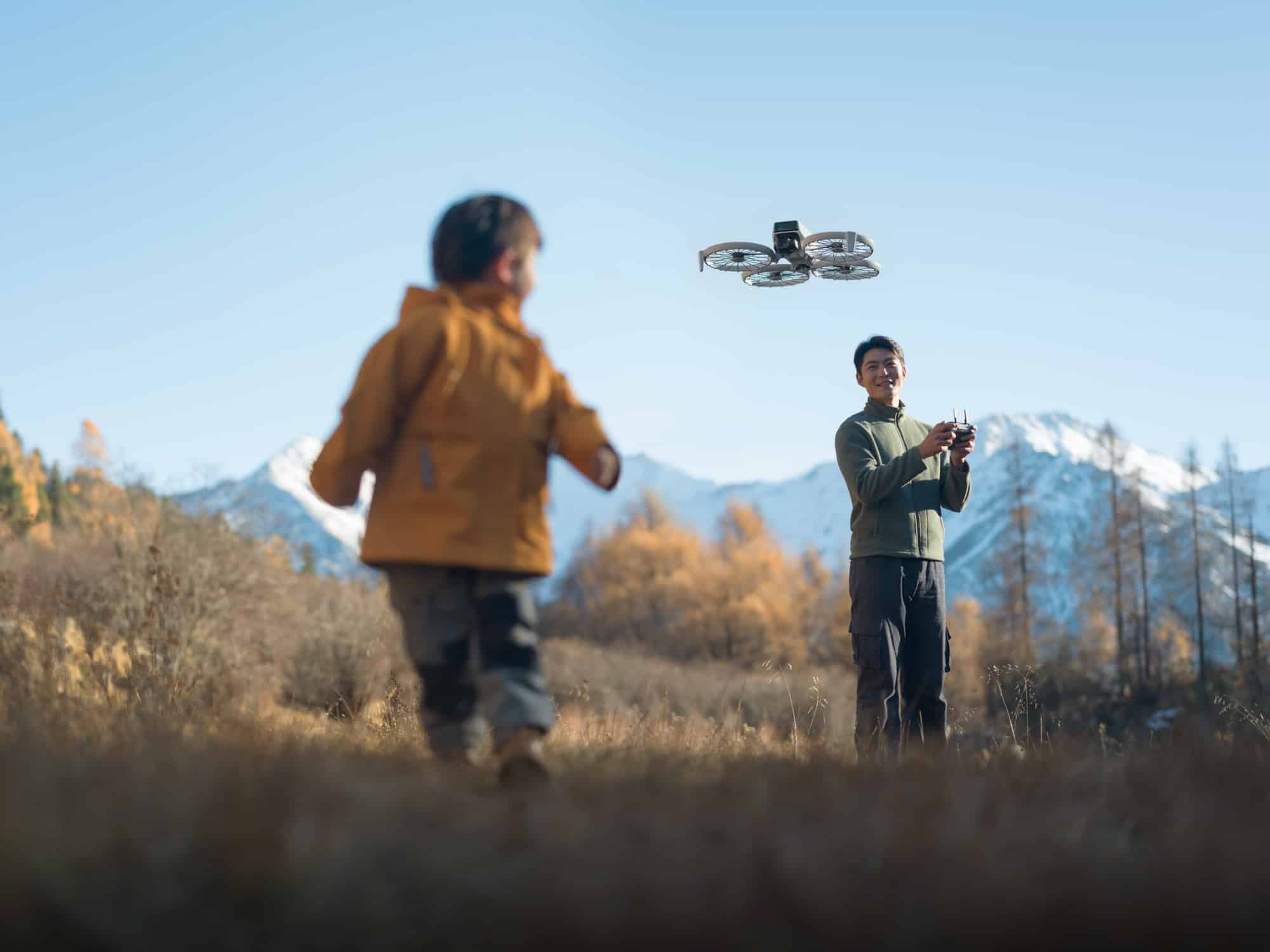Boy running through dry grass while a man flies the Flip behind him.