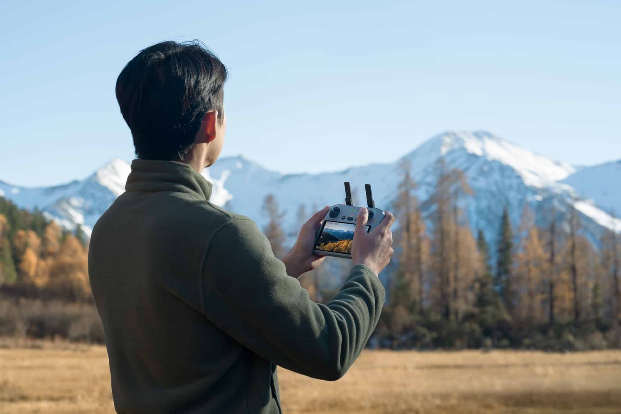 Rear view of a pilot holding the DJI RC 2 showing a live feed.