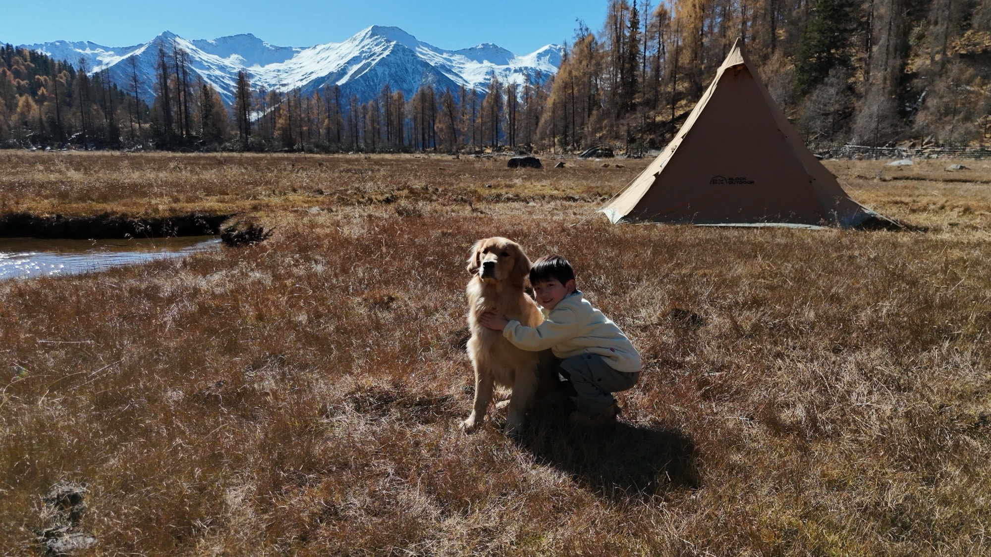 Person hugging a golden retriever beside a teepee tent in a frosty meadow.