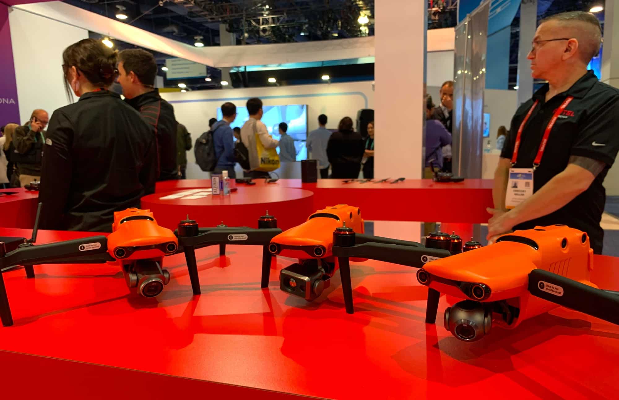 Three orange Autel EVO drones on a red trade show stand with staff nearby.