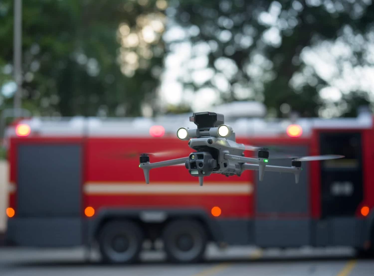 Matrice 4 hovering with spotlights lit in front of a red fire engine.