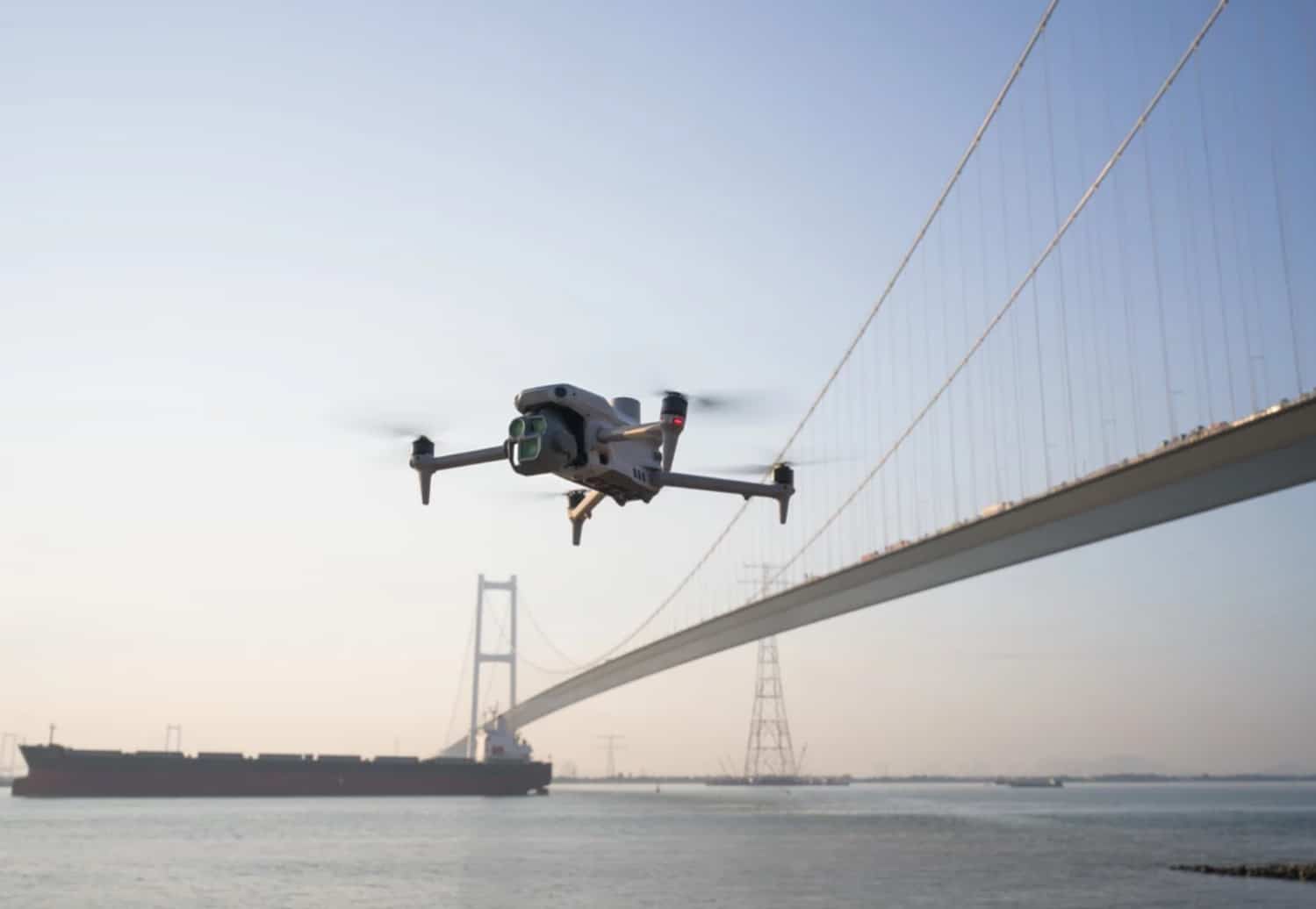 Matrice 4 flying alongside a suspension bridge with a cargo ship below.