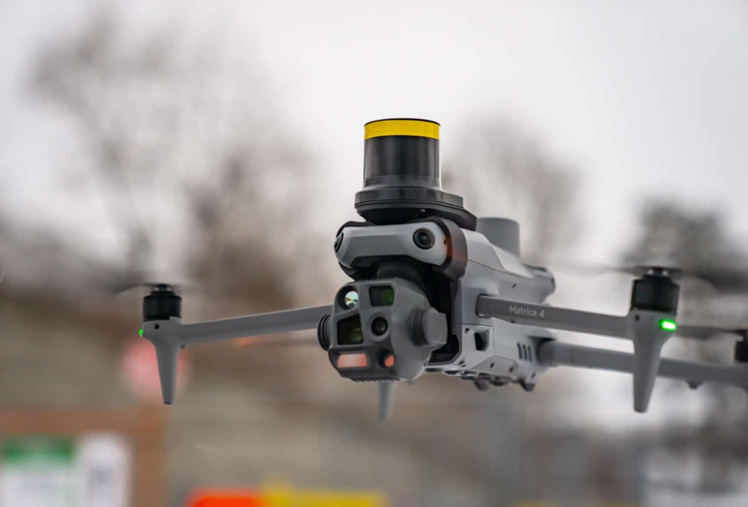 DJI Matrice 4 in flight with a yellow AVSS parachute canister mounted on top.