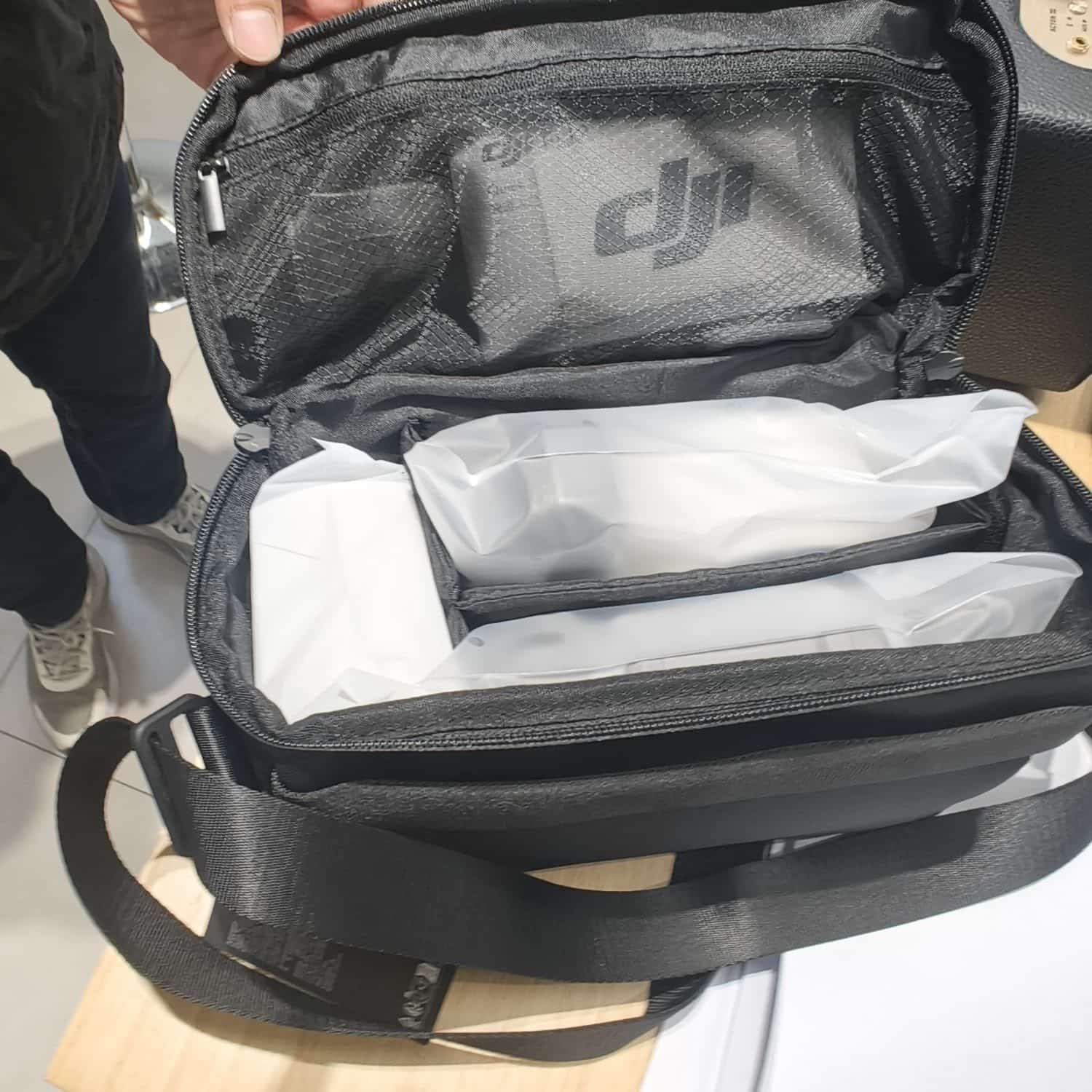 Open grey DJI shoulder bag revealing bagged accessories in its padded compartments.