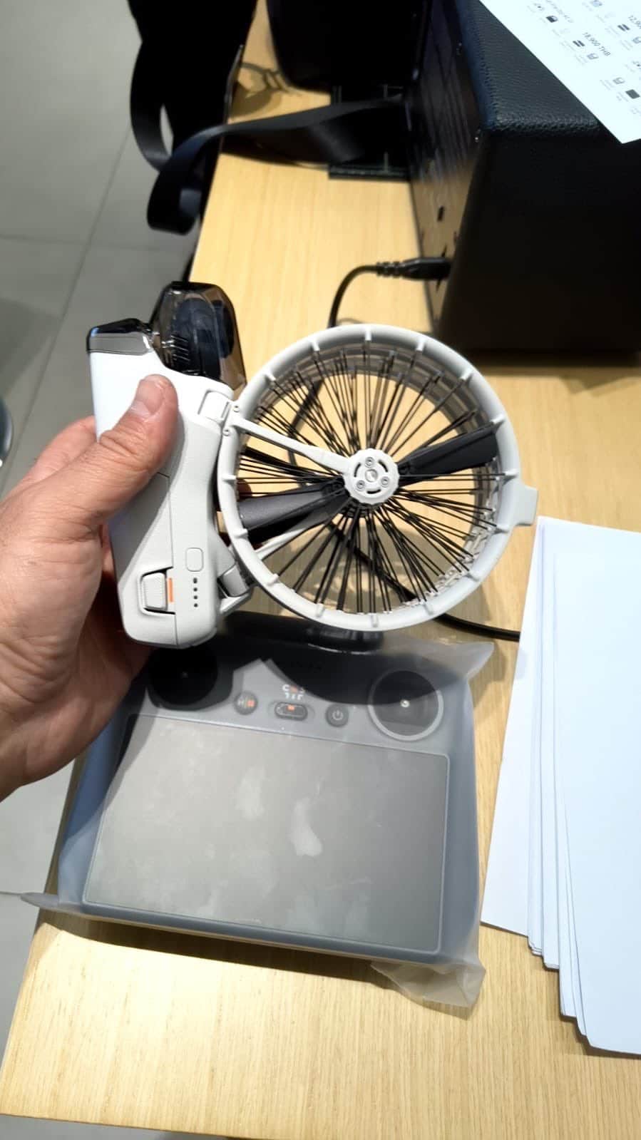 Hand raising the folded Flip above a DJI RC 2 controller inside a shop.