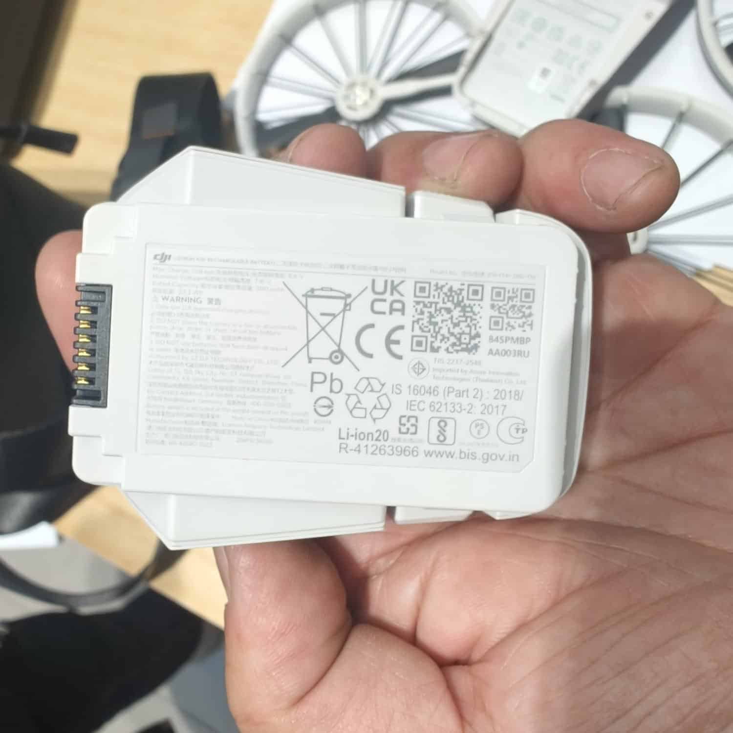 Hand holding a white Flip battery showing its regulatory label and QR code.