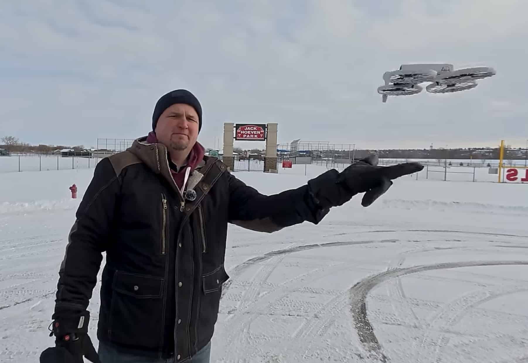 Pilot in a winter coat reaches toward the DJI Flip above a snowy field.