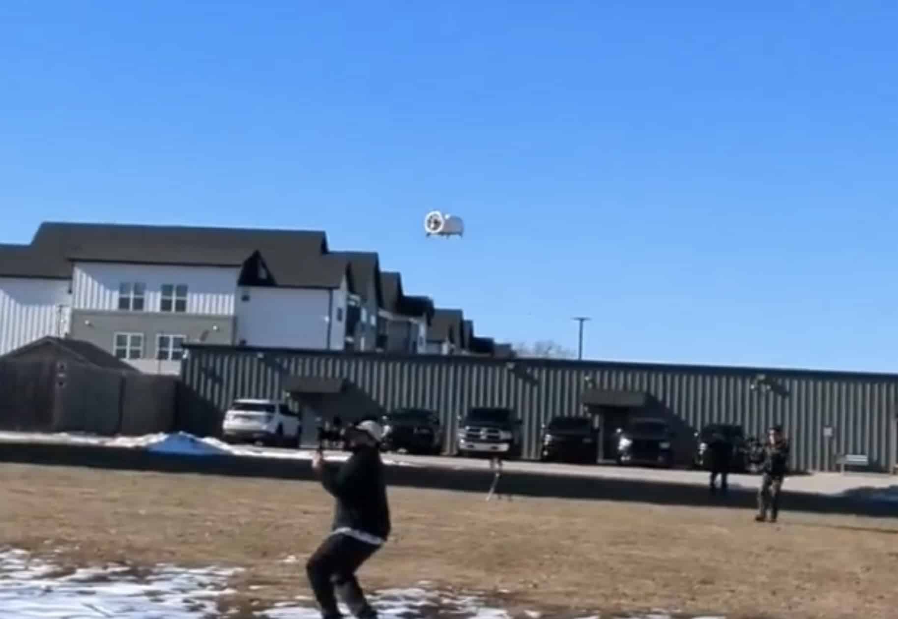 Zipline droid descending on a tether toward a person in a snowy yard.