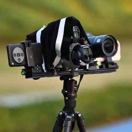 A camera test rail on a tripod aligns a smartphone, drone and mirrorless body under a hood.